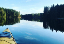 Utsikt over en innsjø omkranset av skog, med fotografen sittende i en kajakk